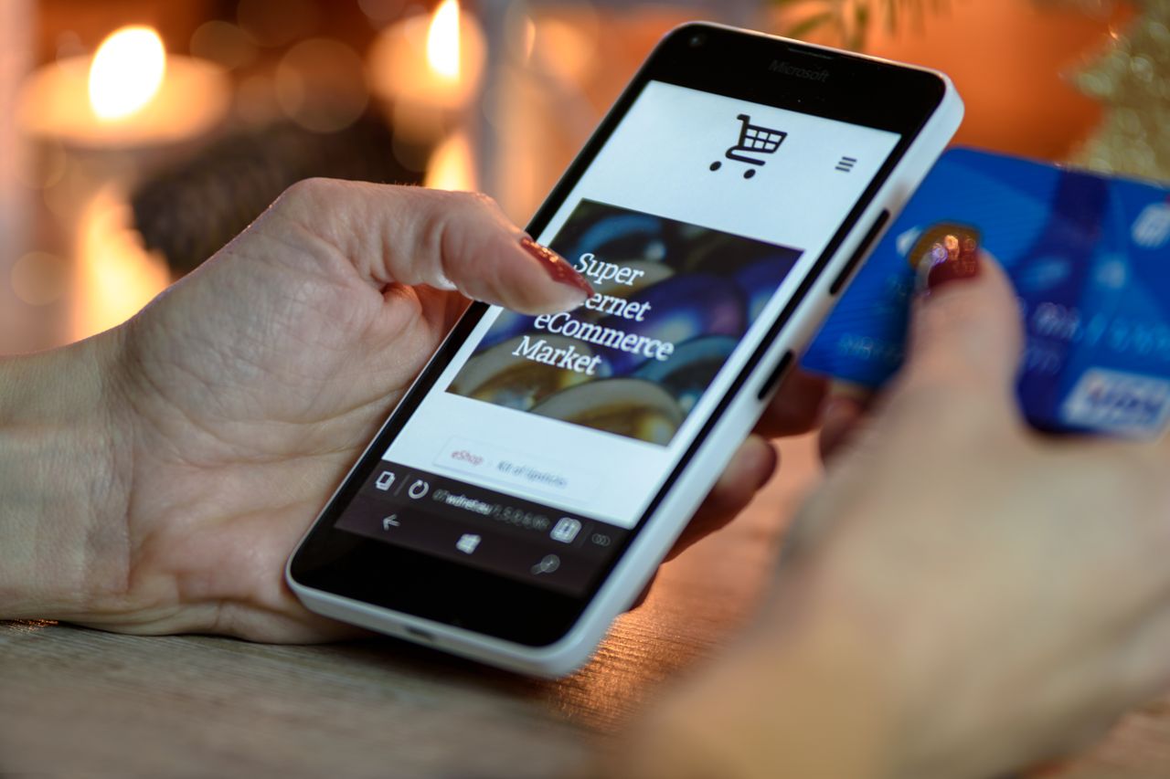 team-01 Woman using smartphone for online shopping with credit card in hand, festive background lighting.
